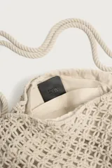 Bolso de hombro confeccionado en tejido trenzado de algodón con diseño de macramé, asa de hombro con detalle de nudo y bolsillo interior plano.