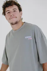 Remera color crema de corte holgado, con cuello redondo y estampado pequeño en el pecho con la frase 'Karma Club' en azul y rojo.