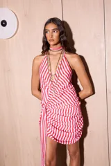 Vestido corto con diseño a rayas rojas y blancas, escote halter pronunciado, drapeado en la cadera y un lazo integrado que cuelga al costado.