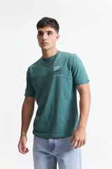 Remera de manga corta color verde azulado, con escote redondo y fit regular. Presenta un estampado gráfico en la espalda con texto "MISTRAL HOUSE PARTY 9/03" y un diseño de manos sosteniendo copas de vino y un disco de vinilo.