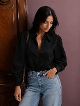Camisa negra de corte clásico con cuello camisero, cartera frontal con botones y mangas largas con volumen y puños con detalle de ondas.