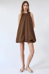 Vestido mini marrón de corte evasé con diseño tipo globo en el dobladillo, cuello redondo y mangas sisa. Presenta bolsillos laterales ocultos en la costura y cierre en la espalda con pequeña abertura y botón.