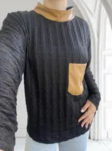 Polera negra de tejido trenzado con cuello alto y bolsillo de cuero color camel.