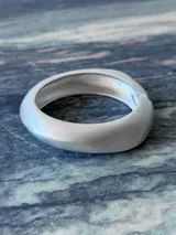 Pulsera rígida de metal plateado con forma oval irregular y acabado mate.