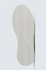 Zapatilla deportiva blanca con suela de plataforma gruesa y texturizada. Presenta detalles en gamuza gris en el lateral y un parche negro en el talón.