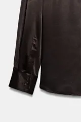 Camisa de cuello solapa y manga larga, confeccionada en tejido satinado de acabado fluido. Presenta cierre frontal con botones y bajo asimétrico.