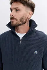 Sweater de punto acanalado en color marrón oscuro, con cuello alto y cierre frontal de cremallera parcial. Presenta mangas largas y puños ajustados.