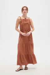 Vestido largo de algodón color blanco, con tirantes finos ajustables con lazos en los hombros, escote recto decorado con apliques florales tridimensionales, cordón ajustable en la cintura y falda larga con volados horizontales.