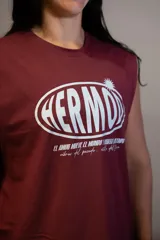 Musculosa sin mangas color bordó con cuello redondo. Estampado frontal en blanco con la palabra "HERMD" en un óvalo con efecto 3D y texto pequeño debajo que dice "el amor mueve el mundo y hasta el olimpo vibras del pasado. estilo del futuro".