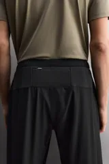 Pantalón de jogging negro confeccionado en tejido técnico ligero y elástico, corte slim fit, con cintura elástica ajustable con cordón, bolsillos laterales y trasero con cierre de cremallera, bandas reflectantes en las piernas y bajos ajustables con cremallera.