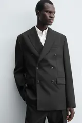 Blazer de corte regular confeccionada en tejido de lana italiana. Presenta cuello con solapas de pico, cierre frontal de botonadura cruzada, manga larga con puños abotonados, bolsillos de vivo en el pecho y bolsillos de solapa en la cadera.