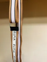 Correa para cartera regulable con diseño de franjas en color tostado, blanco y negro, con la marca Rupia estampada en la sección blanca.