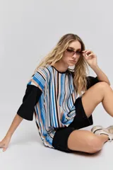 Remera oversize de manga corta con diseño de rayas verticales en tonos rojos, negros, blancos y tostados, y mangas blancas lisas.