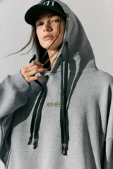 Buzo gris de frisa con capucha, bolsillos delanteros y corte oversize. Tiene recortes laterales, doble cordón con puntera de goma y estampa en frente y espalda.