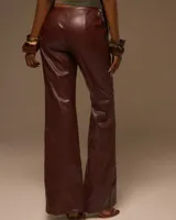 Pantalón largo de cuerina marrón, corte recto y holgado, con múltiples costuras horizontales decoradas con tachas doradas a lo largo de las piernas.