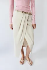 Falda midi de tiro medio color beige, con pliegues en la parte delantera, abertura frontal en el bajo y cinturón combinado a tono con hebilla metálica.