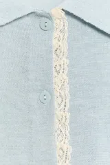 Chaqueta de punto celeste de manga corta con cuello polo, cierre frontal con botones y detalles de puntilla en color beige en la botonera y los puños.