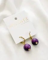 Aros colgantes dorados con esferas de color púrpura. El diámetro del aro es de 1,5cm y las medidas del colgante son 1,5 x 1,5cm. El material del aro es acero.
