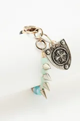 Pulsera de diseño artesanal compuesta por una combinación de cuentas de vidrio en tonos rojizos y negros, intercaladas con piezas metálicas. Presenta un dije central en forma de escudo con detalle de cruz grabada y cierre de mosquetón.