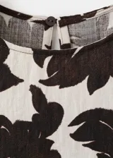 Blusa crop fluida de cuello redondo y sin mangas, con estampado floral en tonos marrones sobre base beige y detalles de lazos ajustables en los laterales.