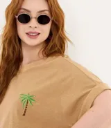 Remera de algodón texturizado color camel, con cuello redondo, manga corta con bajo plegado y un pequeño bordado de palmera en el pecho.