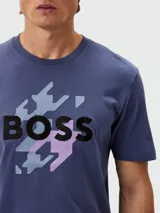 Remera de algodón azul con cuello redondo y manga corta. Presenta un estampado frontal con la palabra "BOSS" en negro, superpuesta sobre un patrón abstracto en tonos celestes, grises y rosados.
