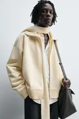 Sudadera color crema de algodón con interior afelpado, corte relajado, cuello subido y manga larga. Presenta bolsillos de vivo en la cadera y acabados en rib, con cierre frontal de cremallera.