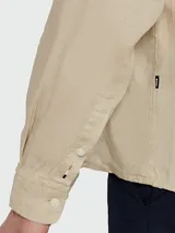 Camisa de vestir color beige claro, de corte clásico, con cuello abotonado y mangas largas.