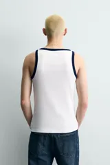 Camiseta sin mangas slim fit color blanco, con cuello redondo y sisas ribeteadas en azul marino. Estampado frontal con la palabra "League" y el número "'86" en azul marino.