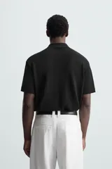 Polo negro de manga corta con cuello solapa y abertura frontal. Presenta un tejido jacquard con textura geométrica sutil.