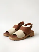 Sandalias de cuero combinadas en color marrón y crudo, con suela track y taco bajo. Tienen tira ajustable con hebilla en el talón.