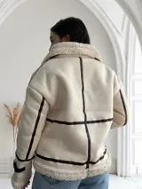 Chaqueta color crudo con interior de piel sintética color beige, cierre frontal con cremallera y un bolsillo de cuero marrón en el pecho.