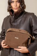 Cartera de gamuza color marrón con diseño estructurado, solapa superior decorada con tachas metálicas doradas y placa metálica con el logo de la marca en el centro.