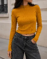Remera de morley color mostaza, de manga larga y ajuste al cuerpo. Presenta cuello alto con terminación fruncida y bordes ondulados en puños y ruedo.