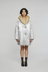 Campera reversible de corte regular, confeccionada en nylon con acabado repelente al agua. Presenta diseño con capucha, mangas raglán y cierre frontal con botones. Un lado es de color negro con bolsillos de parche, mientras que el reverso es de color plateado con bolsillos laterales integrados.