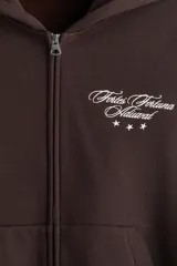 Campera canguro de felpa marrón oscuro, con cierre frontal completo, capucha, bolsillos delanteros tipo parche y pequeño bordado blanco en el pecho con texto y estrellas.