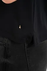 Remera negra de viscosa y elastano, con cuello redondo y mangas cortas con volados. Tiene un corte holgado y un pequeño detalle metálico dorado en el bajo.