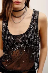 Top de malla transparente en color negro con aplicaciones de lentejuelas y abalorios formando patrones de hojas en el frente, tirantes finos y escote redondo.