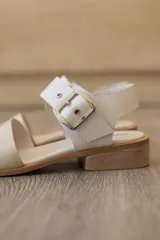 Sandalia plana de cuero color suela, con capellada lisa en la parte delantera y tira trasera con textura de reptil en tonos marrones y naranjas. Cuenta con una hebilla metálica grande en el tobillo y taco bajo.