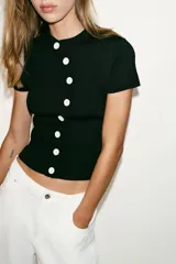 Top de punto negro de manga corta y cuello redondo, con cierre frontal de botones blancos dispuestos de forma asimétrica y ondulada.