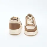 Zapatillas bajas de estilo retro, con paneles en color beige claro y marrón topo. Presentan cordones blancos y suela gruesa de color crema.