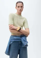 Jersey de punto color verde menta, con diseño de trenzas y detalles calados. Presenta cuello redondo, manga corta y terminaciones elásticas acanaladas.