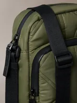 Cartera reporter color verde militar de Calvin Klein, con textura acolchada, costuras con monograma, cierre superior y bolsillo delantero con cremallera. Incluye correa ajustable negra.