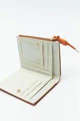 Billetera compacta de símil cuero color celeste claro, con cierre superior y un tirador de cordón trenzado multicolor. Posee un parche frontal con el logo de la marca.