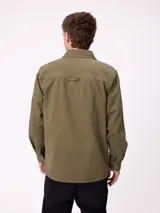 Camisa de gabardina color verde oliva, con cuello clásico, cierre frontal de botones y dos bolsillos frontales con parche. Incluye un pequeño parche con el logo de la marca en el bolsillo izquierdo.