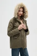 Campera parka de color verde militar, con cierre frontal oculto, bolsillos laterales con solapa y capucha fija con borde de piel sintética.