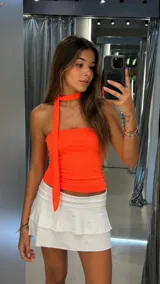 Top strapless color naranja neón, con diseño ajustado y lazo largo integrado al cuello que cae sobre el frente.