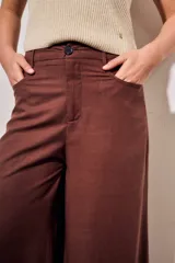 Pantalón marrón de tiro alto y corte recto con piernas amplias, bolsillos delanteros aplicados y cierre frontal con botón.