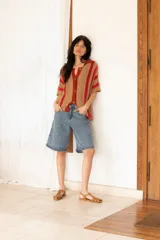 Camisa tejida a rayas horizontales color tostado y rojo, con cuello polo, mangas cortas y botones frontales.