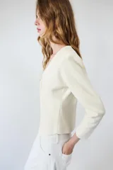Chaqueta de punto color negro, con escote en pico, manga larga y cierre frontal con botones dorados. Presenta un diseño con bajo asimétrico.